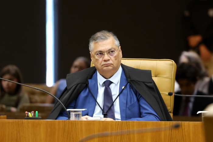 stf-nega-recurso-de-associacao-para-cultivar-cannabis-medicinal Ministro Flávio Dino, do STF, sentado em cadeira de couro dourada durante sessão da 1ª Turma, com toga preta sobre terno azul, óculos e expressão séria, olhando para cima.